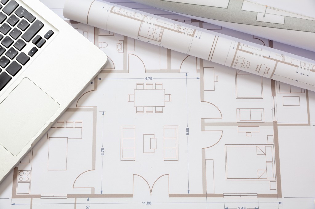 Architectural floor plan on a desk with laptop and rolled blueprints